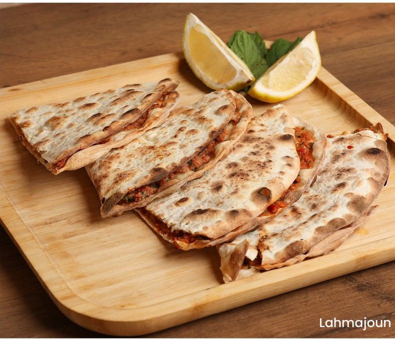 Lahmajun sliced on a wooden board with lemon and mint